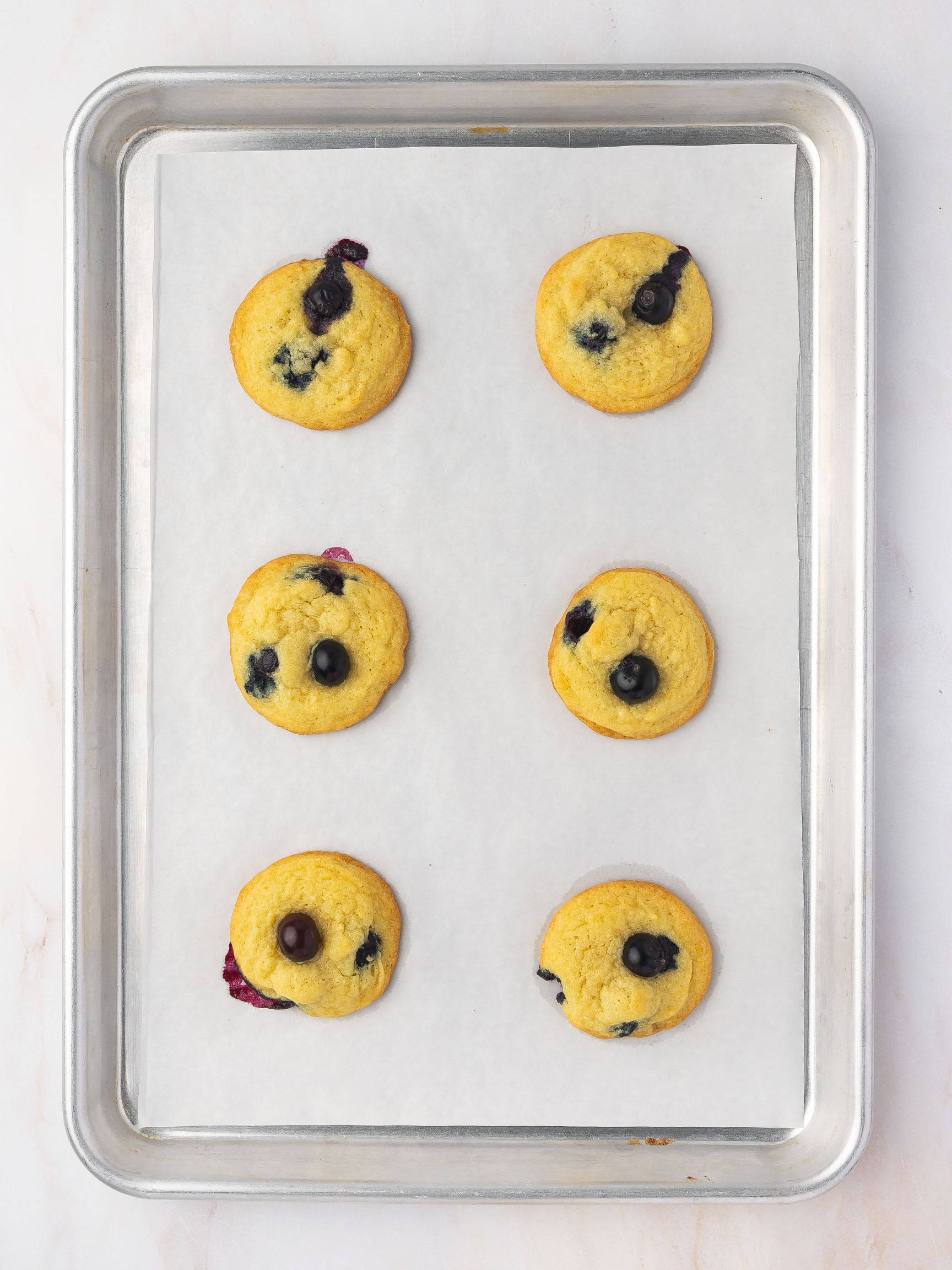 Freshly baked lemon blueberry cookies cooling on a parchment-lined baking sheet straight from the oven.