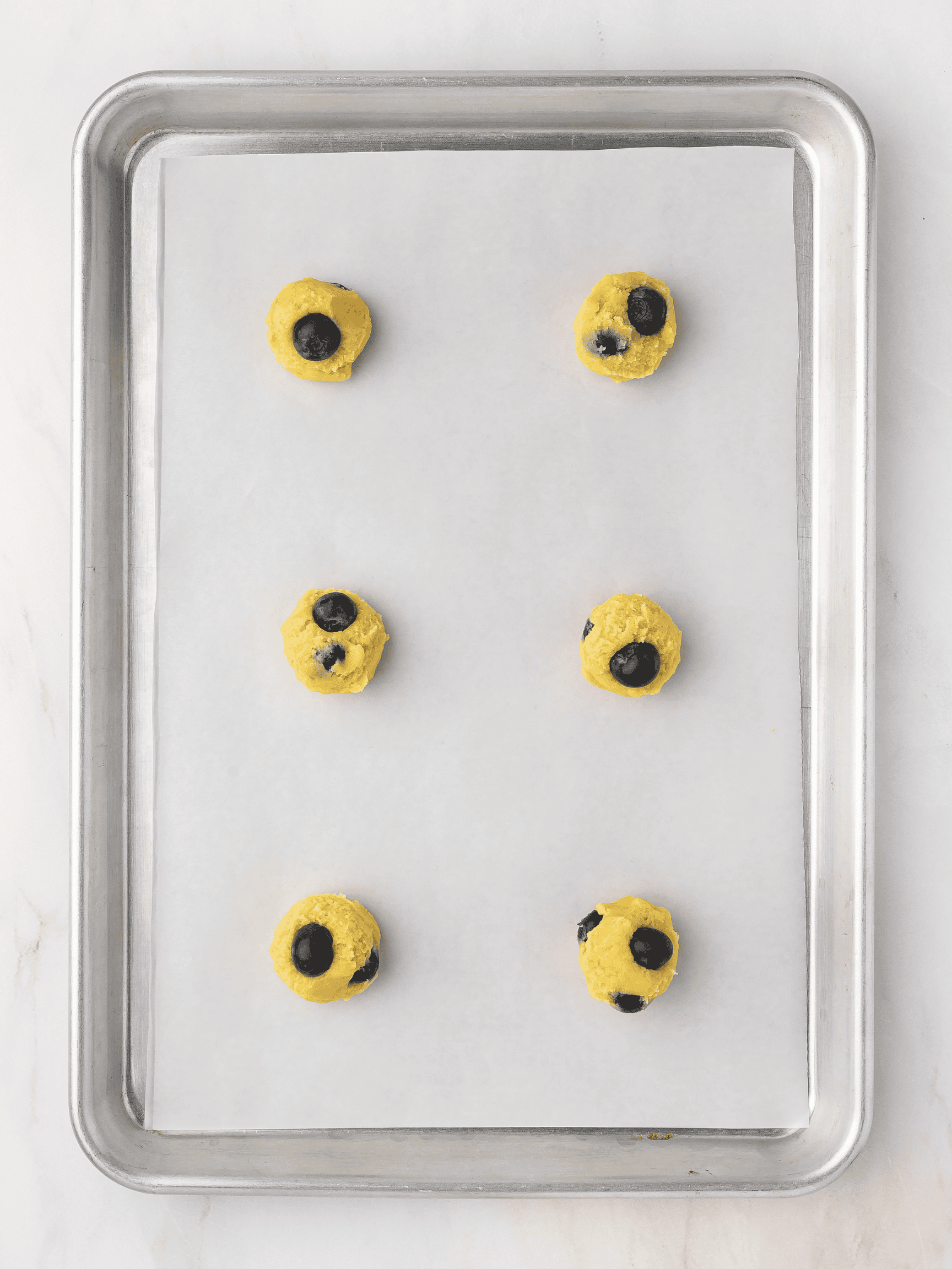 Scooped cookie dough balls placed on a parchment-lined baking sheet, ready to bake into lemon blueberry cookies.