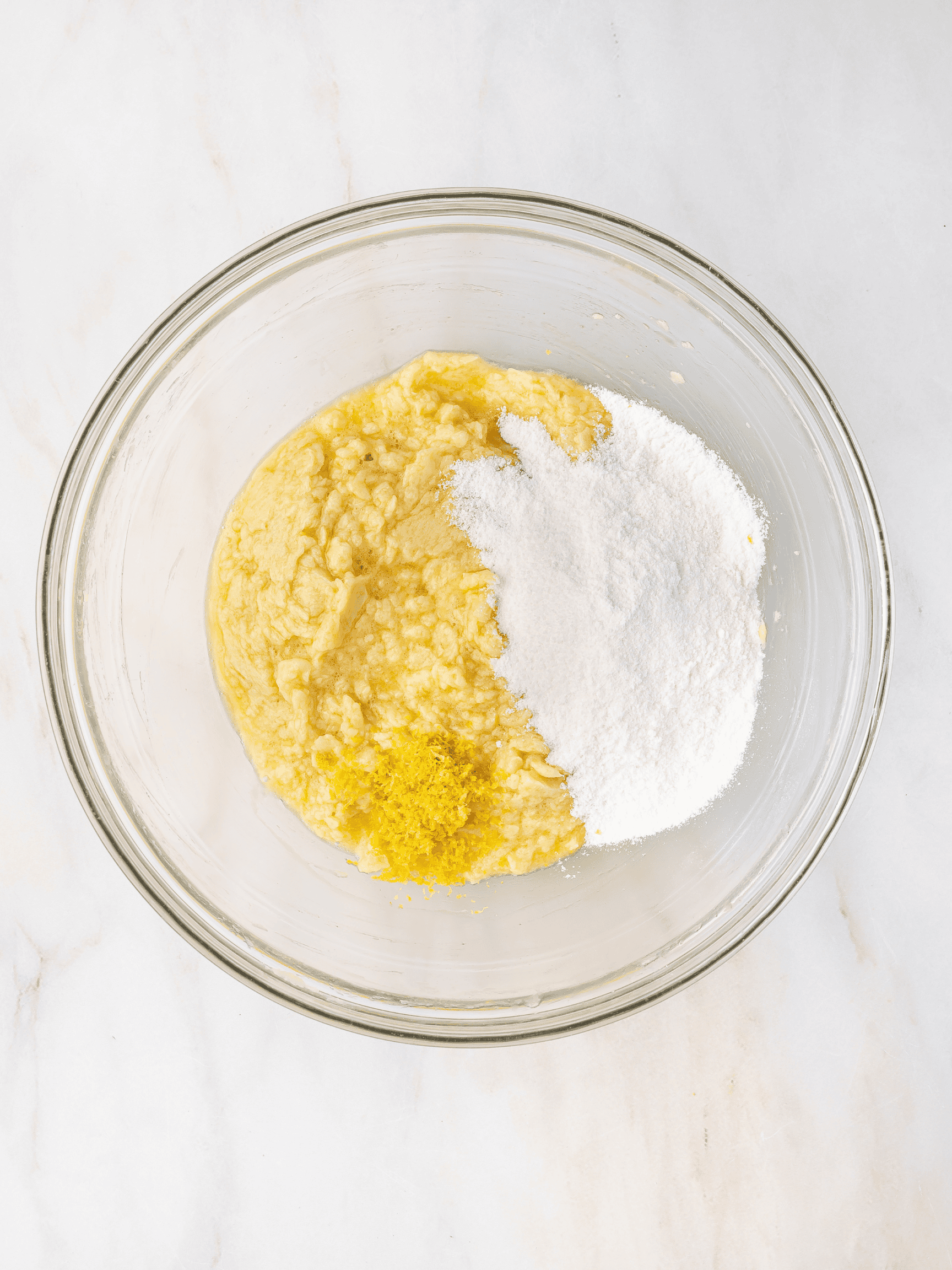 Instant lemon pudding mix being added to the creamed butter, sugar, and egg mixture in a mixing bowl.