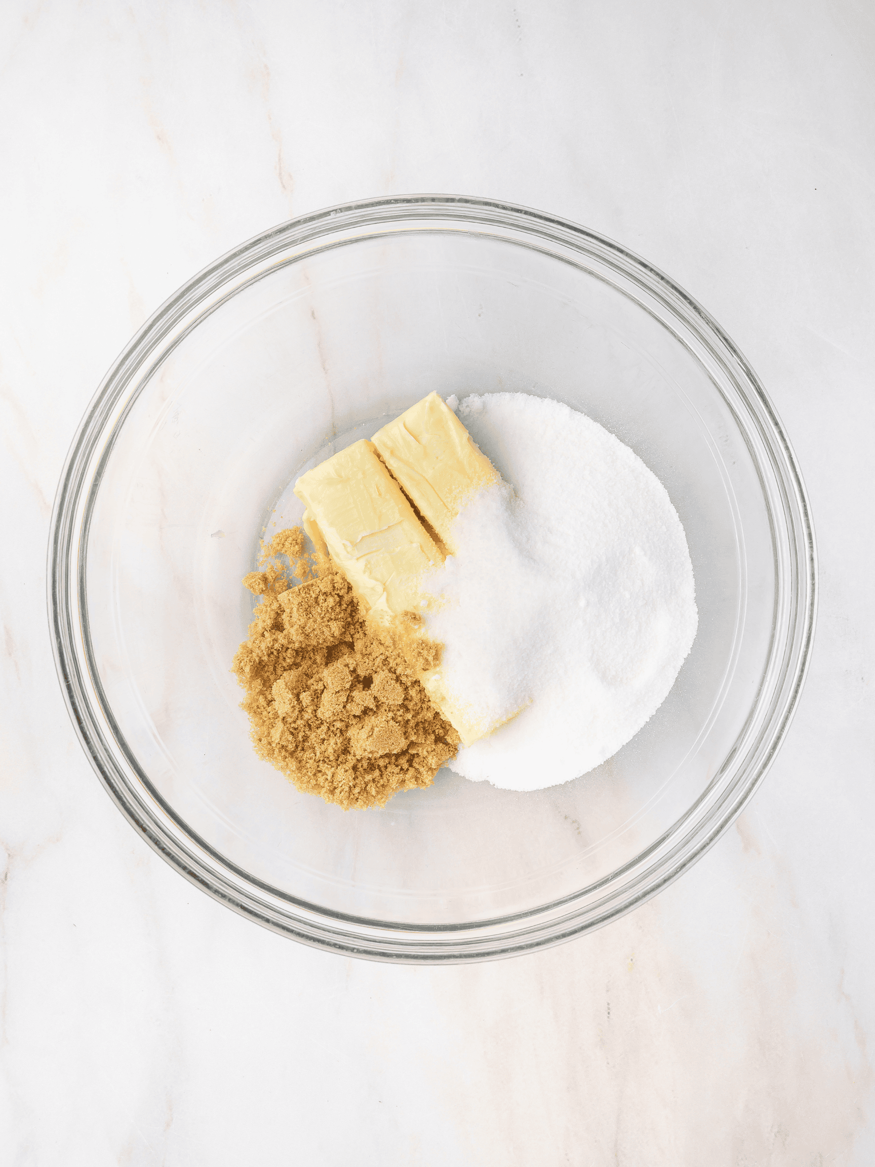 Butter, white sugar, and light brown sugar combined in a glass mixing bowl, ready to be creamed together for baking.