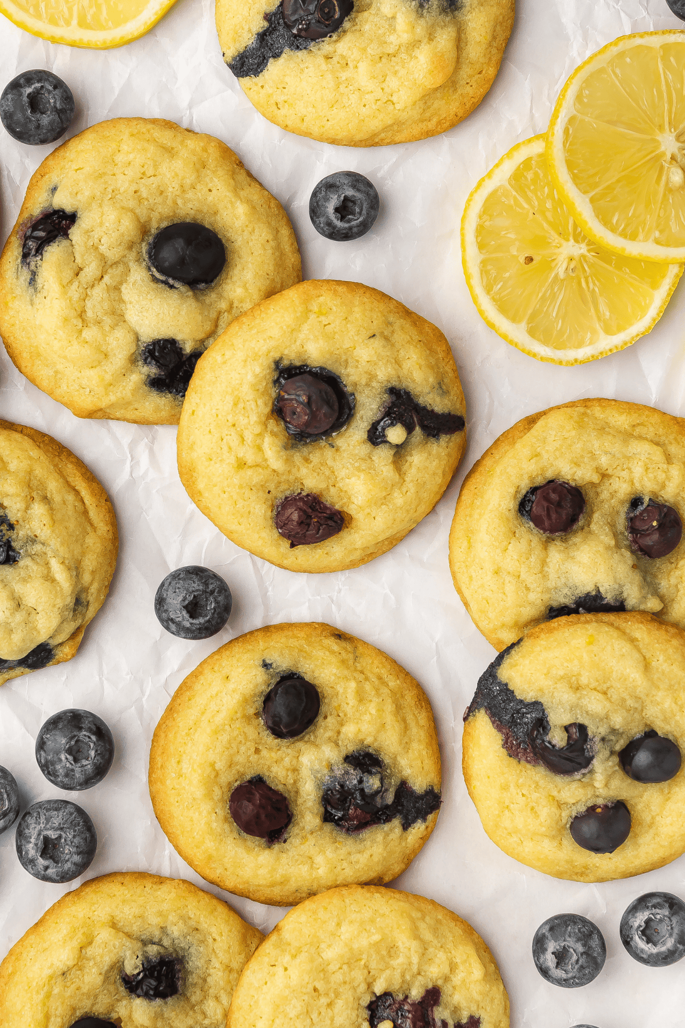 Lemon blueberry cookies scattered on parchment paper with fresh lemon slices at the corner.