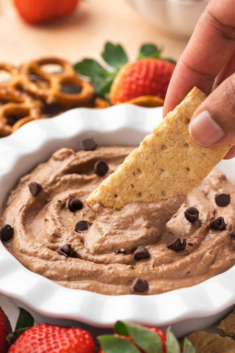 A bowl of creamy brownie batter dip surrounded by various dippers like strawberries, pretzels, apple slices, and graham crackers.