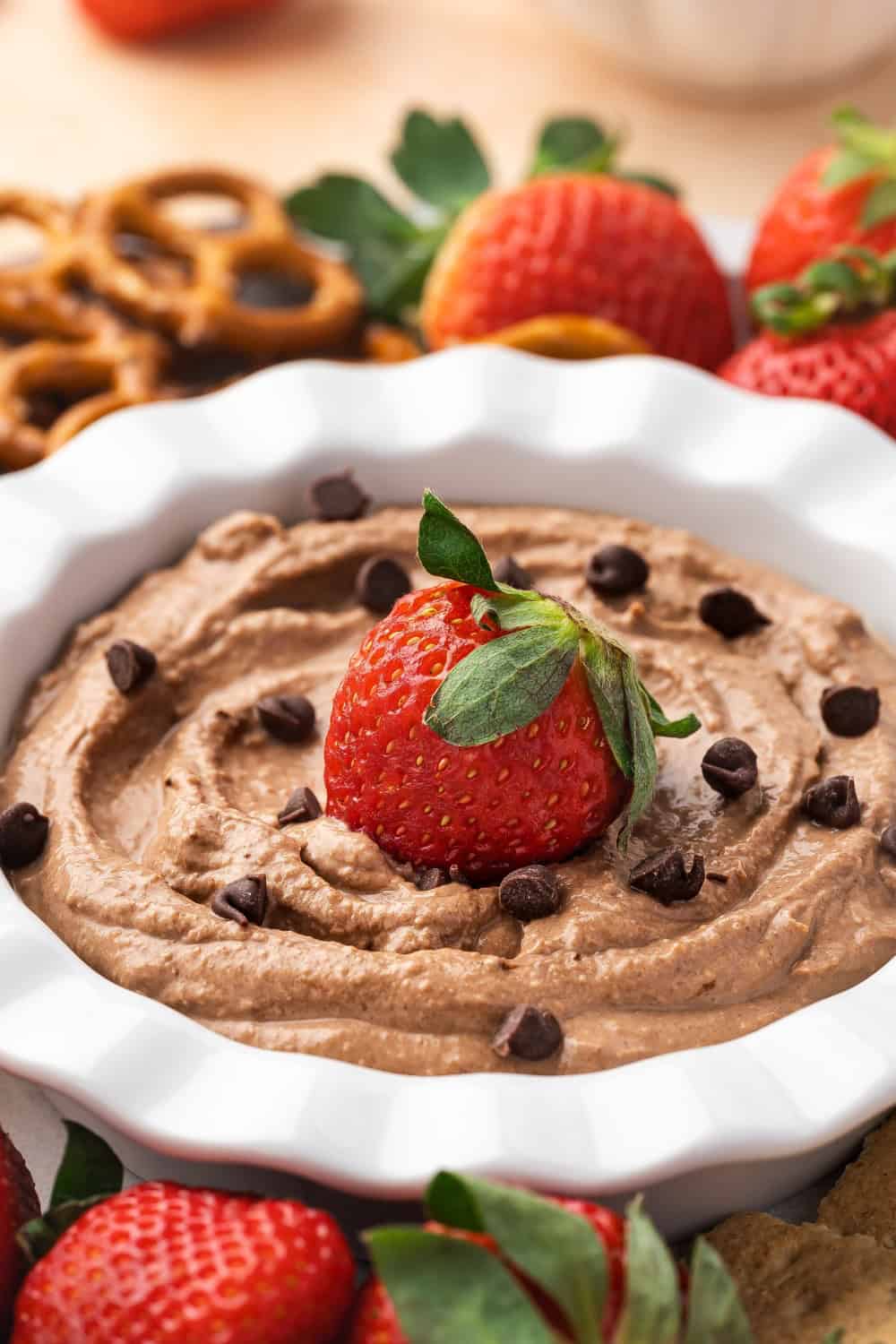 A bowl of creamy brownie batter dip surrounded by various dippers like strawberries, pretzels, apple slices, and graham crackers.