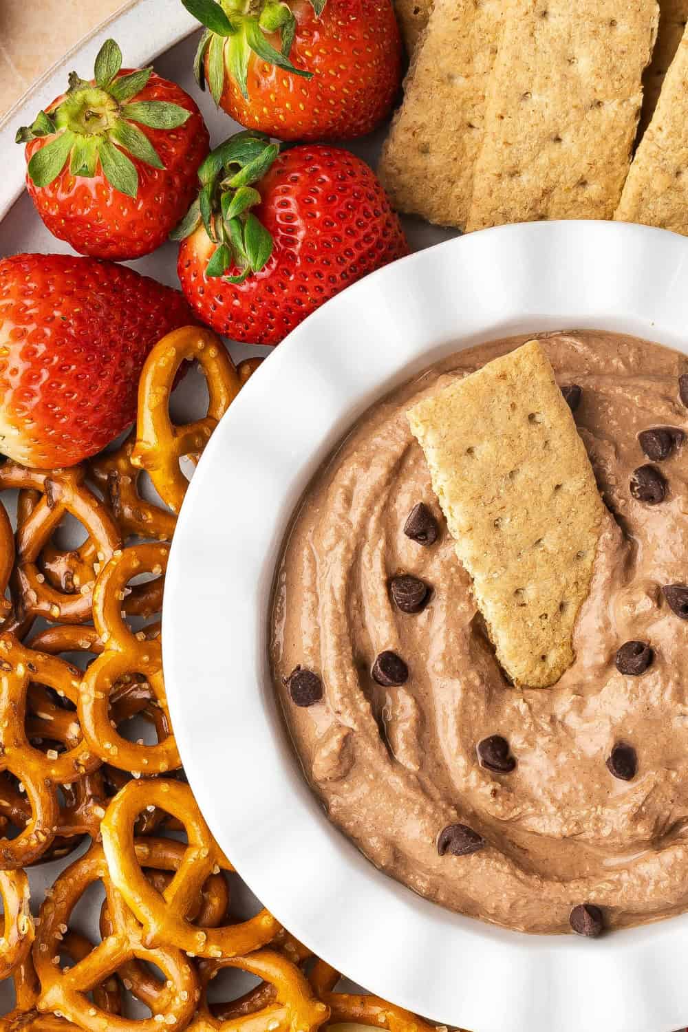 A bowl of creamy brownie batter dip surrounded by various dippers like strawberries, pretzels, apple slices, and graham crackers.