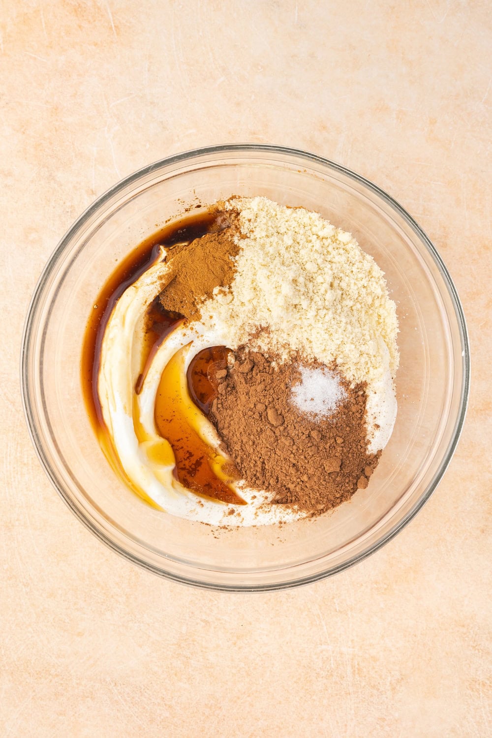 A medium-sized bowl with Greek yogurt, almond flour, cocoa powder, maple syrup, and vanilla extract being mixed into a smooth, creamy consistency.