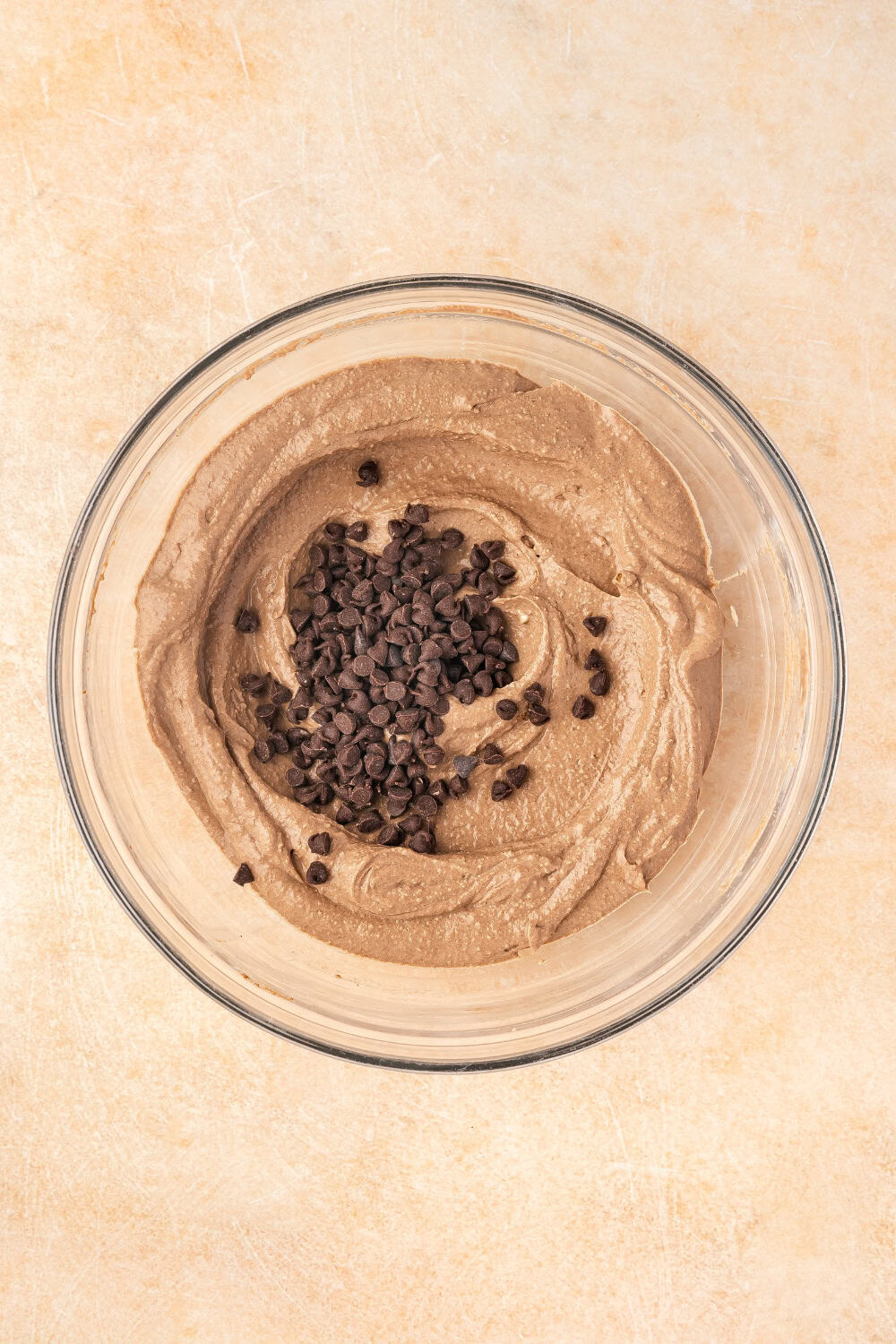 A bowl of creamy brownie batter dip being folded with mini chocolate chips and garnished with additional chocolate chips on top.