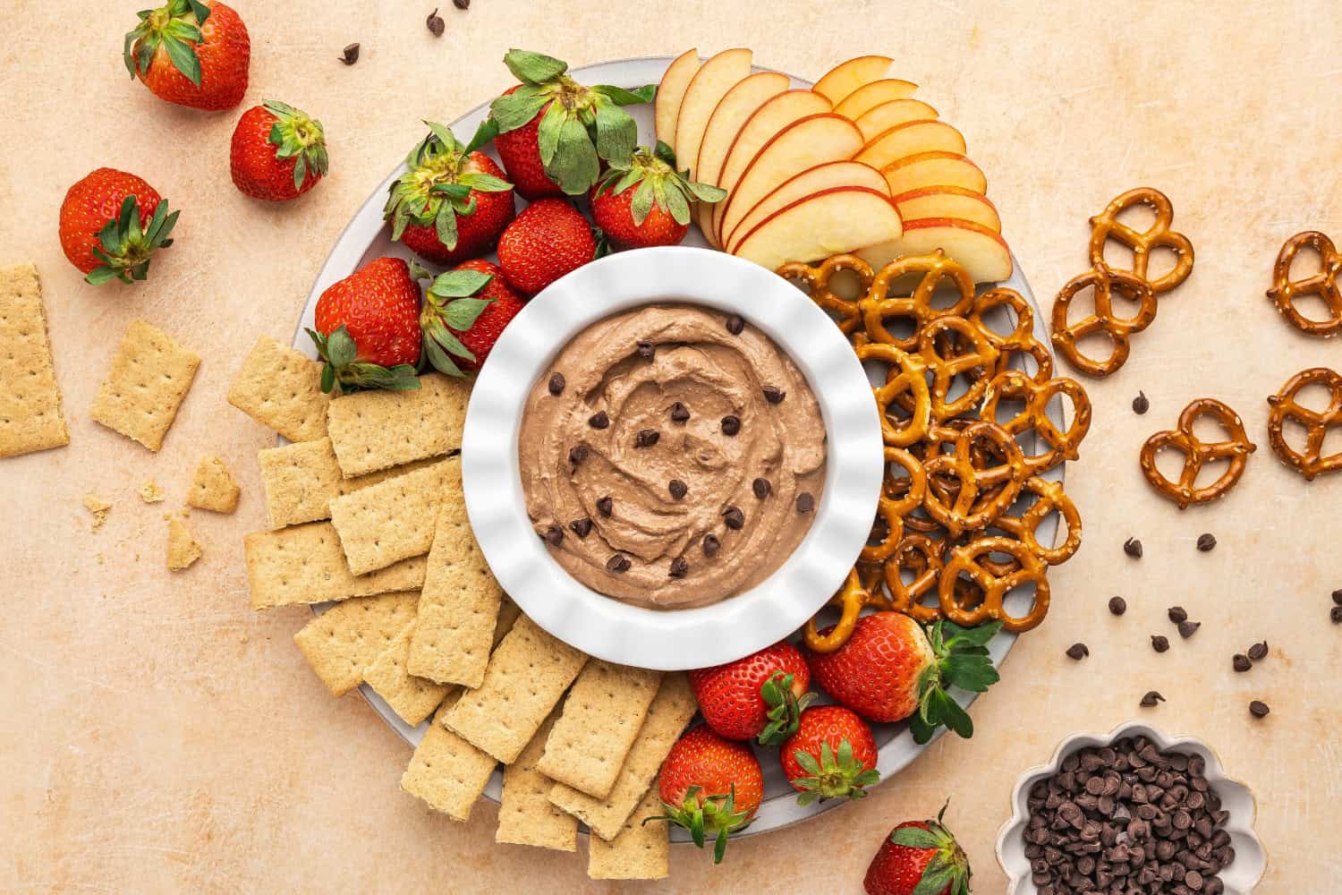 A bowl of creamy brownie batter dip surrounded by various dippers like strawberries, pretzels, apple slices, and graham crackers.