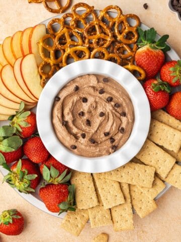 A bowl of creamy brownie batter dip surrounded by various dippers like strawberries, pretzels, apple slices, and graham crackers.