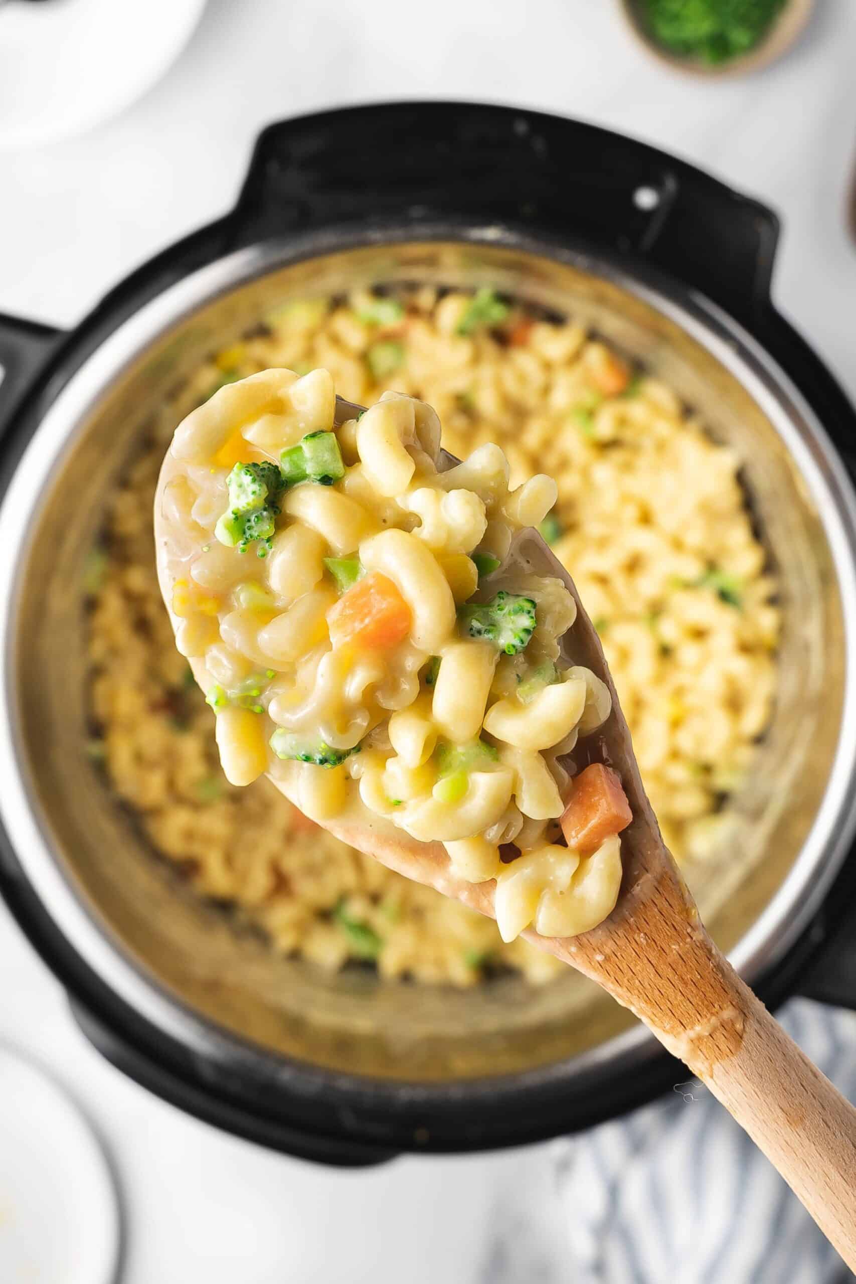 Wooden spoon scooping creamy mac and cheese with vegetables from Instant Pot