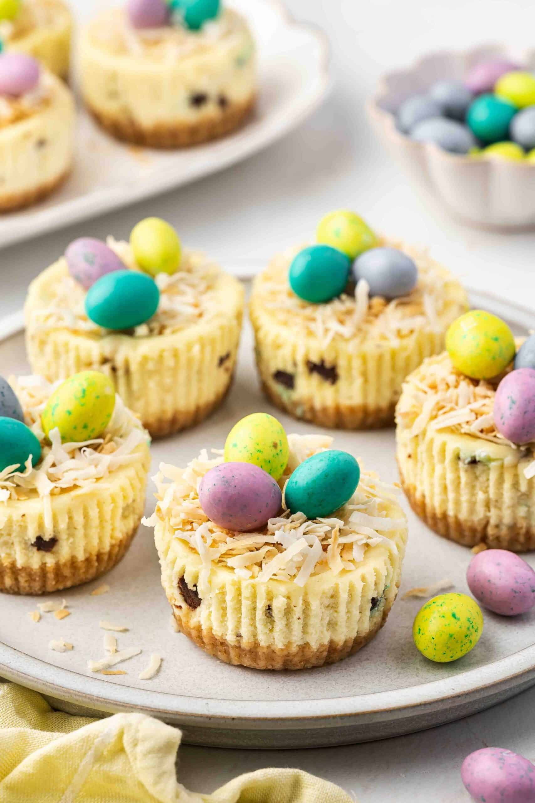 Mini cheesecakes on a decorative plate with candy-coated eggs on top.