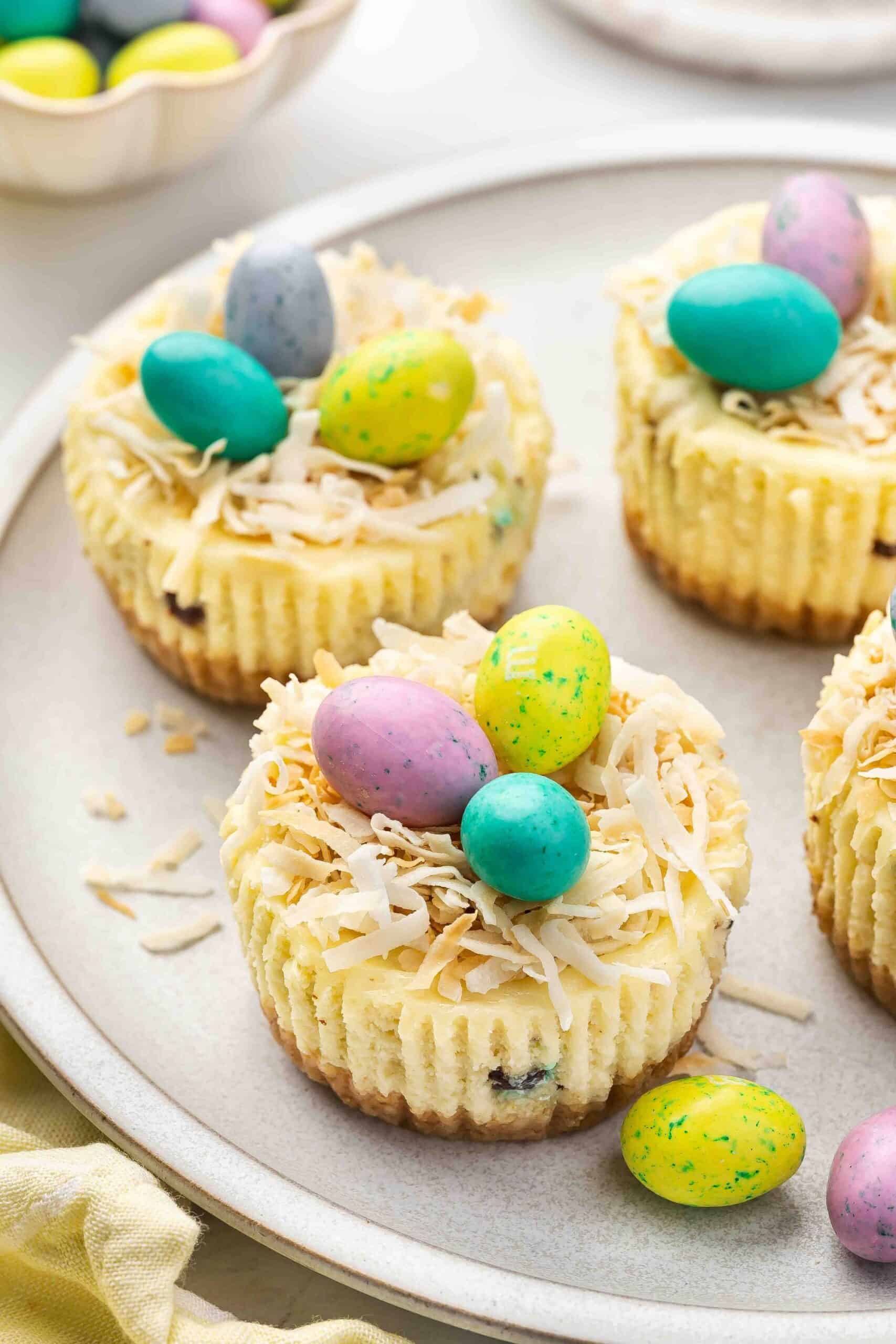 Mini Easter cheesecakes served on a platter with candy-coated chocolate eggs.