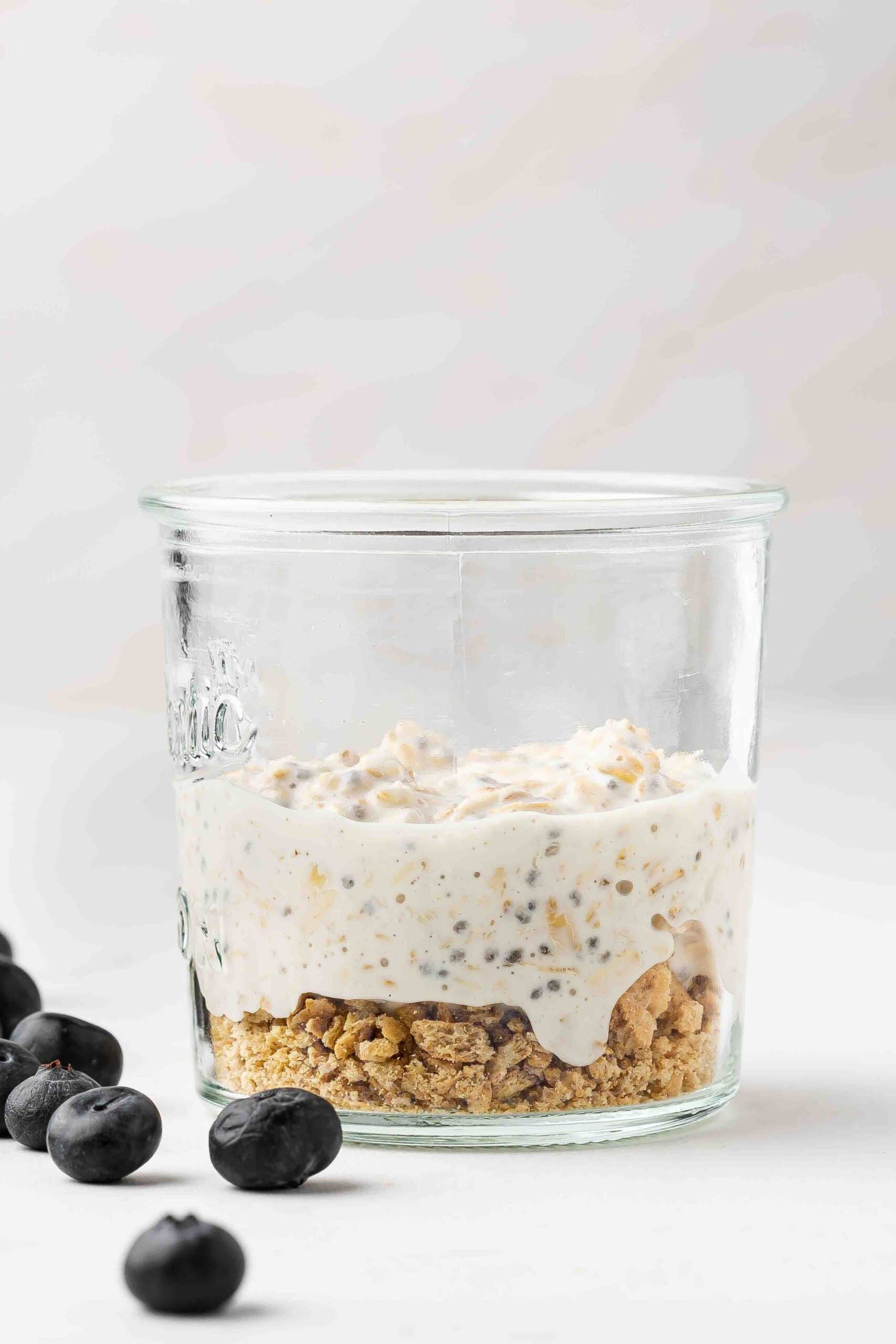 Graham cracker crumbs layered at the bottom of a glass jar, topped with an oats mixture filling half the jar.