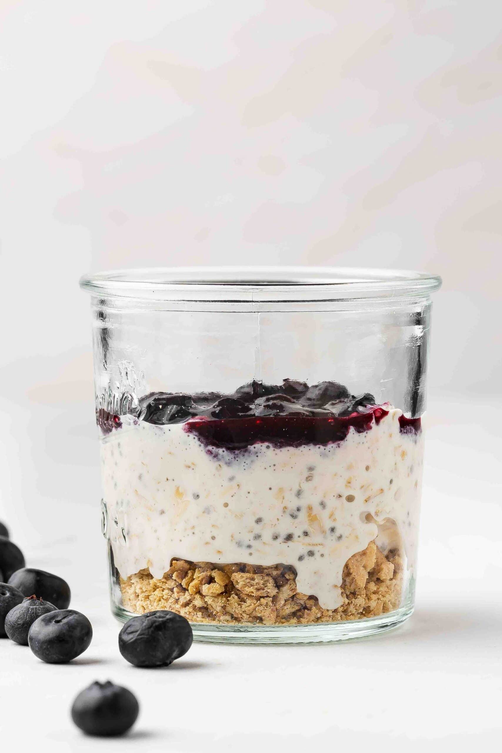 Graham cracker crumbs layered at the bottom of a glass jar, followed by oats mixture and a middle layer of blueberry sauce.