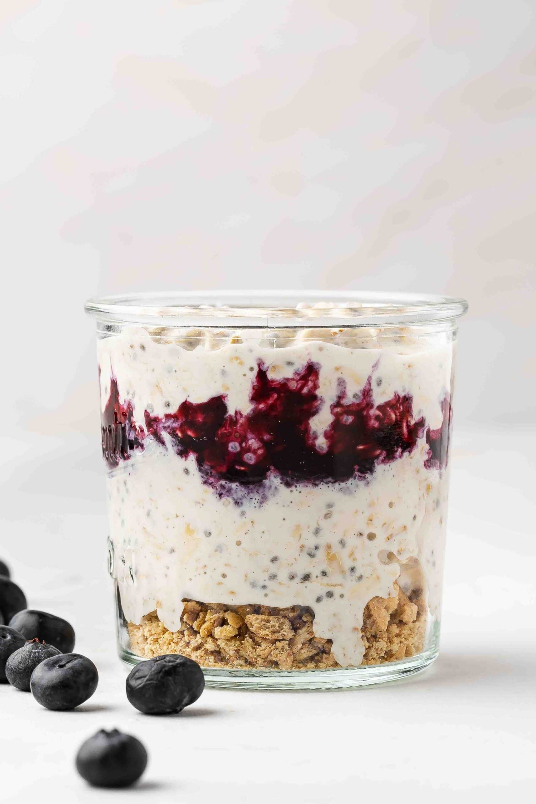 A glass jar layered with graham cracker crumbs, oats mixture, blueberry sauce, and the remaining oats mixture.