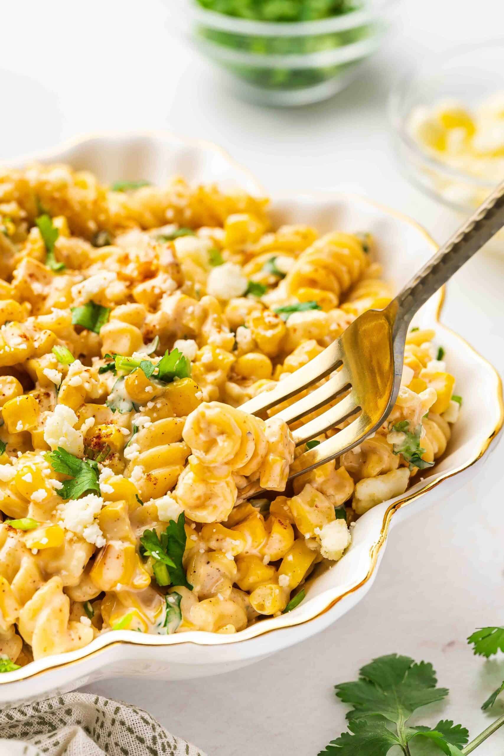 A fork lifting a scoop of street corn pasta salad, showing creamy sauce and cotija cheese crumbles.