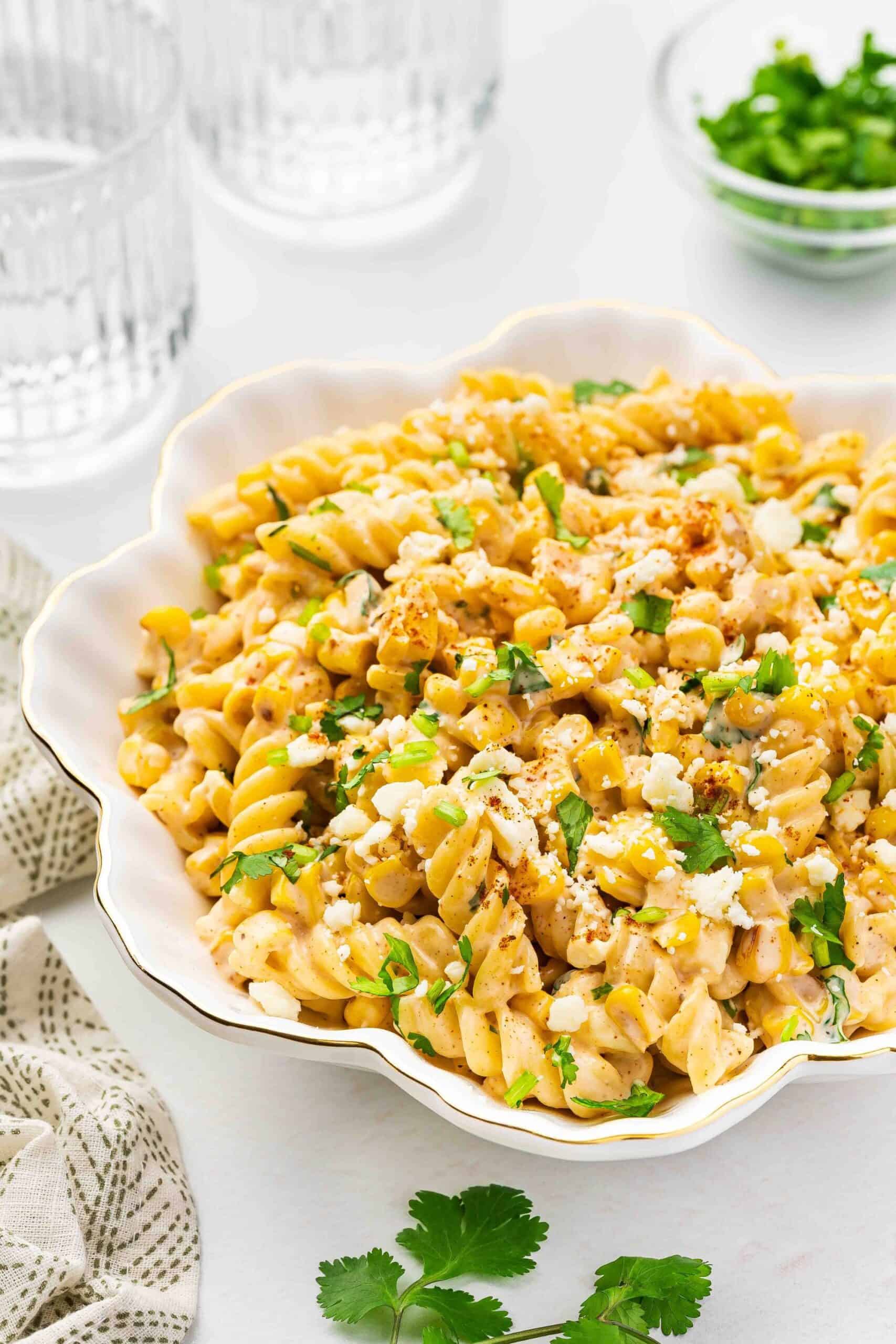 A close-up of a bowl of street corn pasta salad with a bite missing, showing creamy pasta and roasted corn.