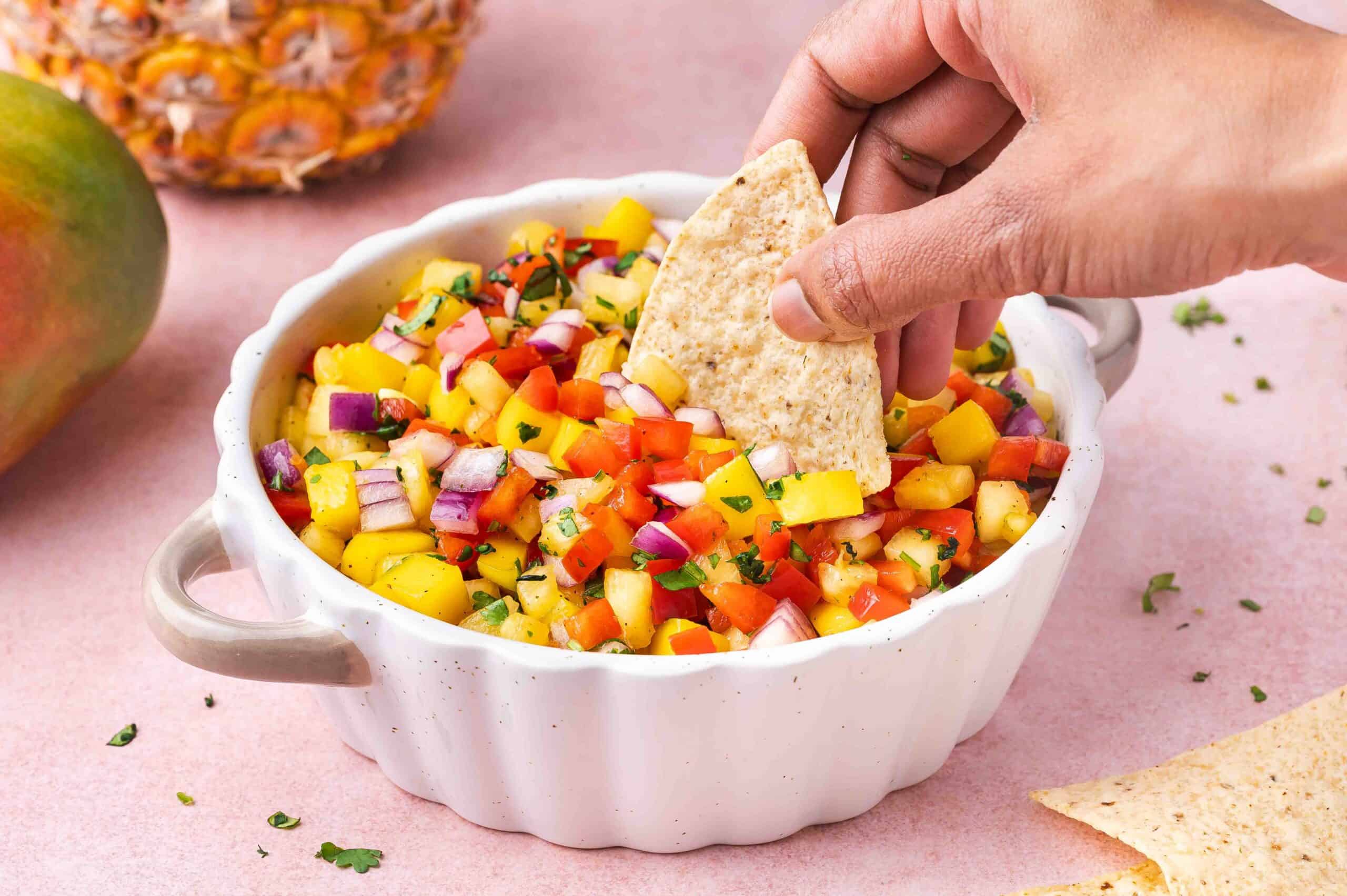 Scooping Mango Pineapple Habanero Salsa from a bowl with a chip.
