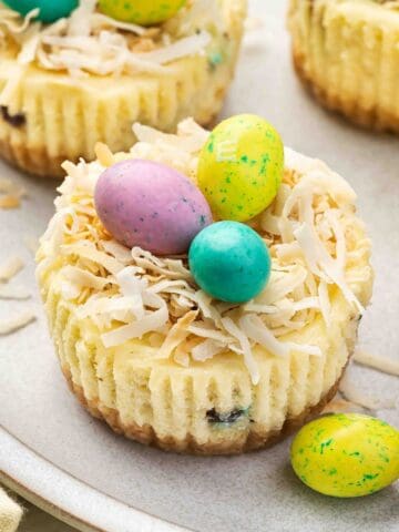 Mini Easter cheesecakes arranged on a decorative serving plate with bright candy eggs on top.