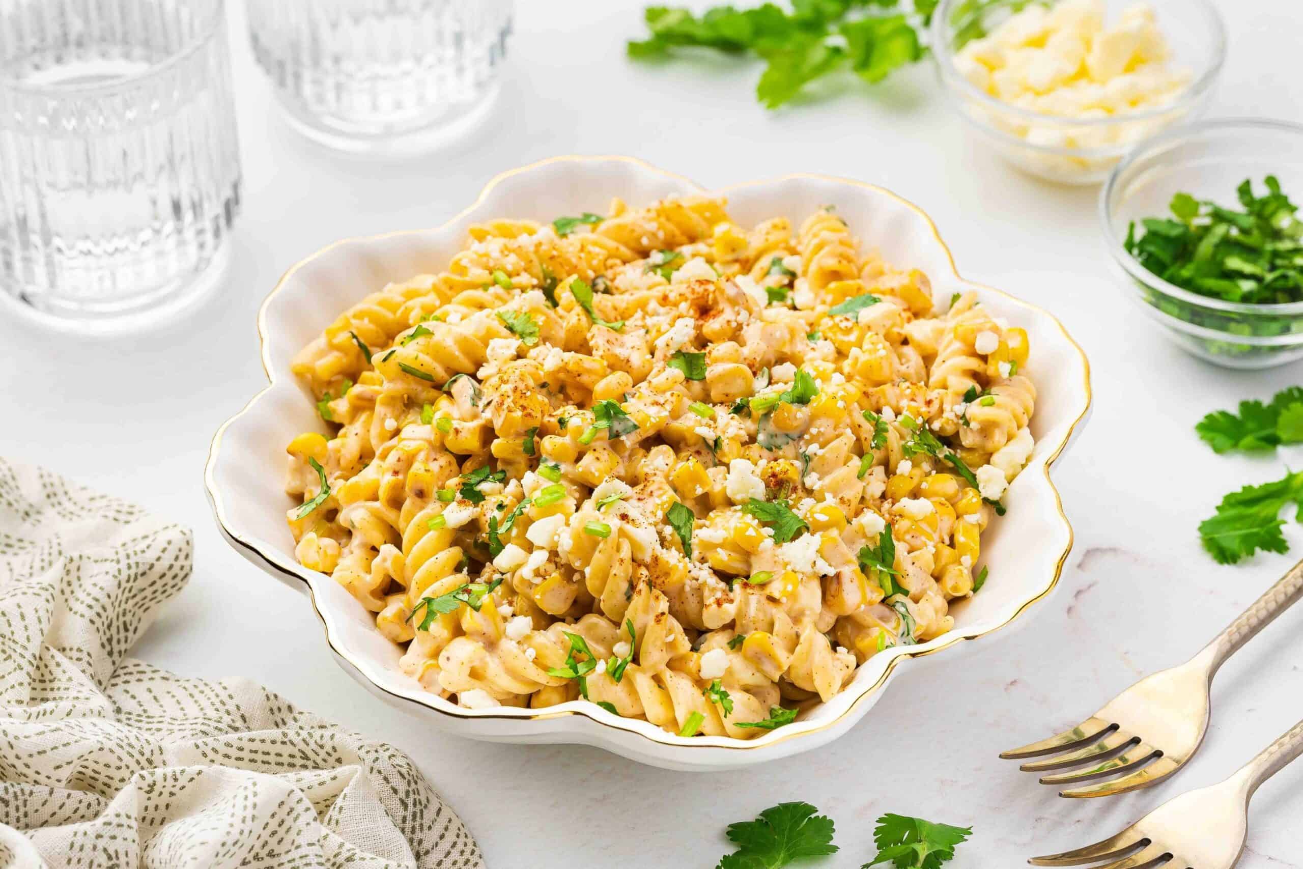 A side-angle view of a bowl filled with creamy street corn pasta salad, topped with fresh cilantro and cotija cheese.