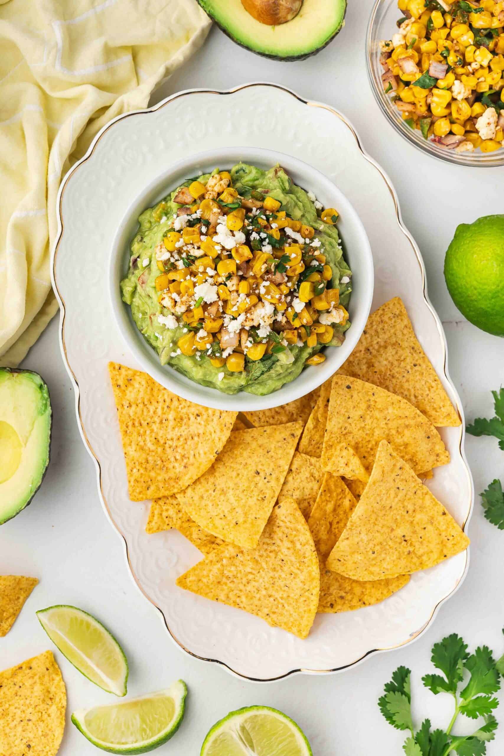 Platter with Mexican street corn guacamole and tortilla chips, garnished with cilantro.