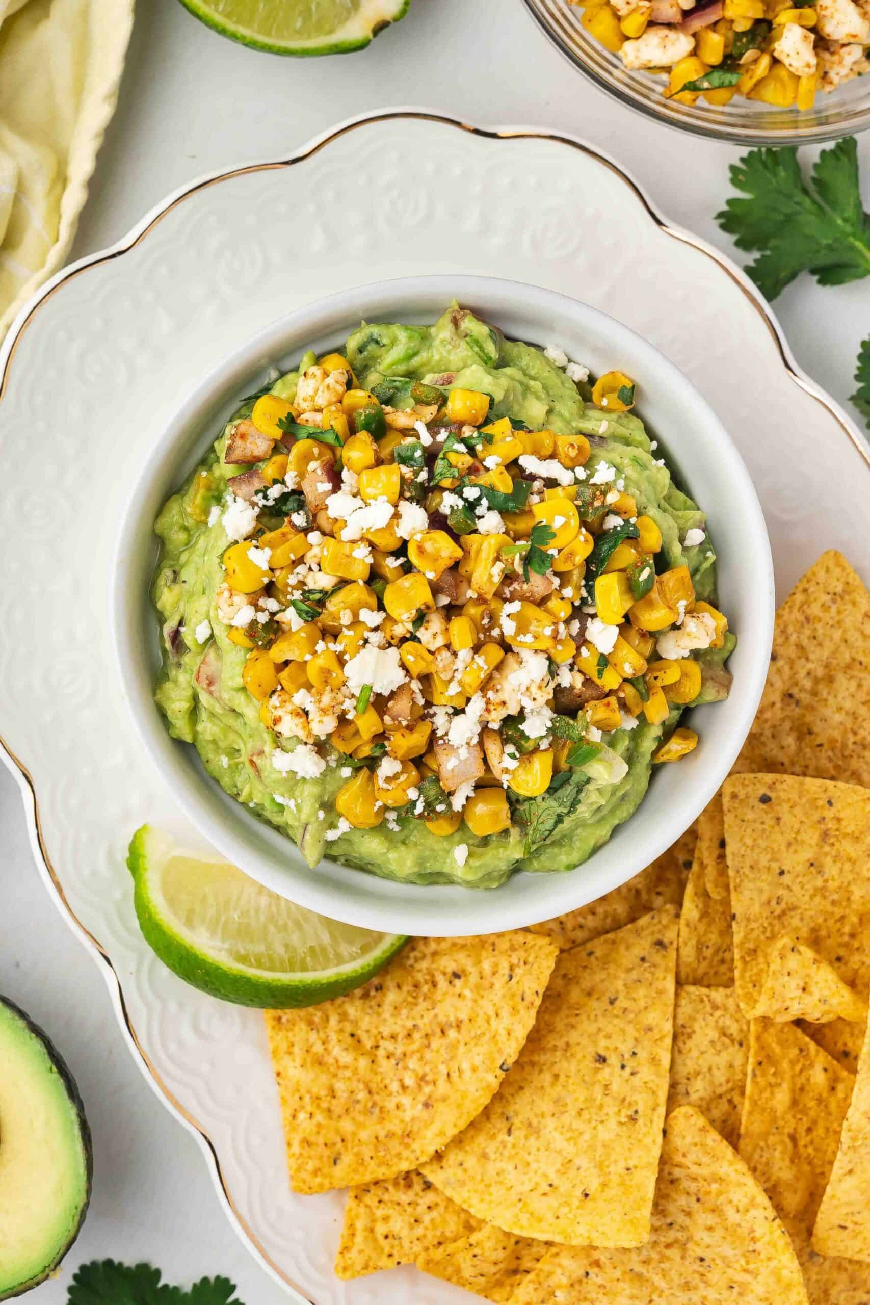 Close-up of Mexican street corn guacamole served with a side of tortilla chips and lime wedges.