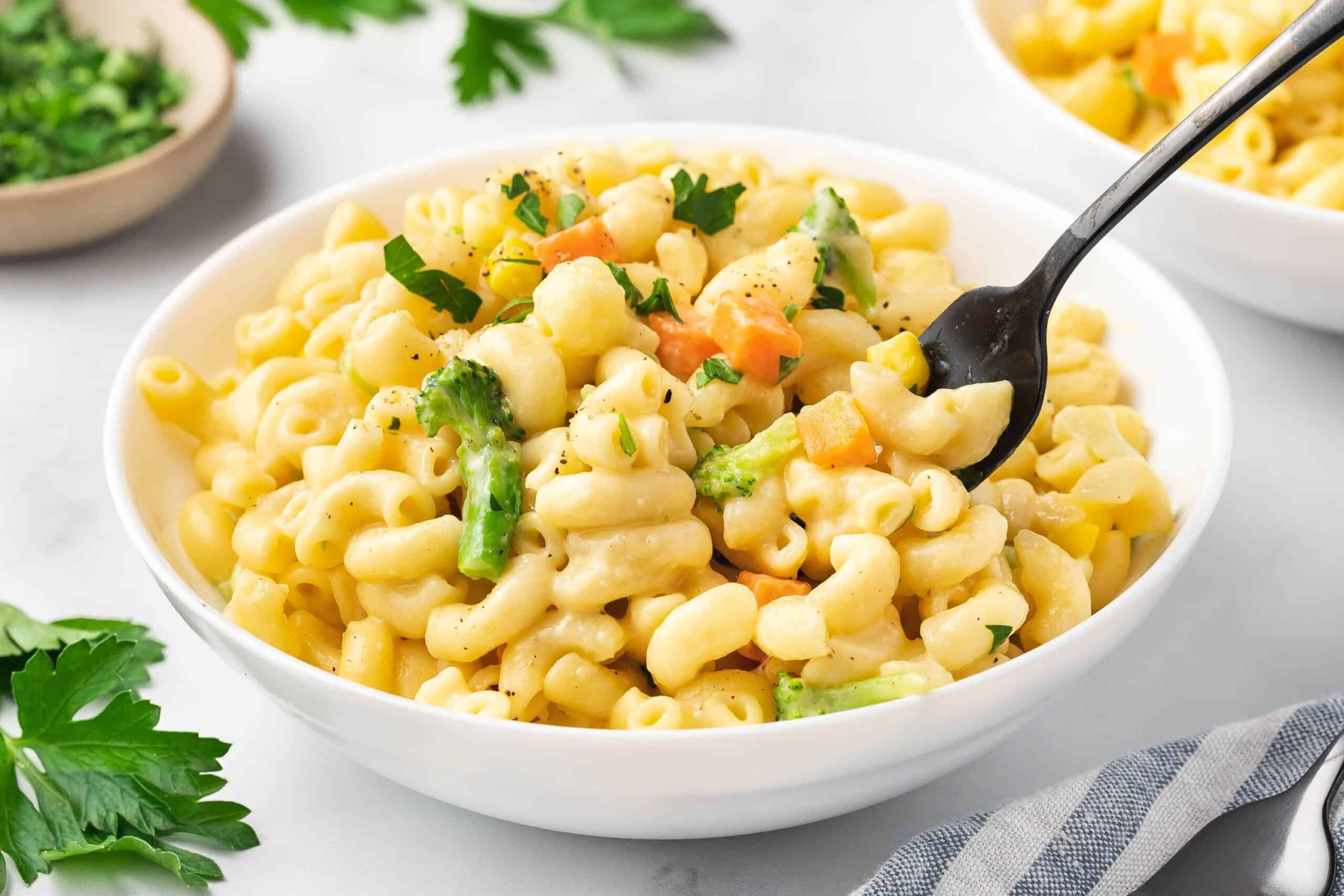 Fork scooping mac and cheese with mixed vegetables from a bowl