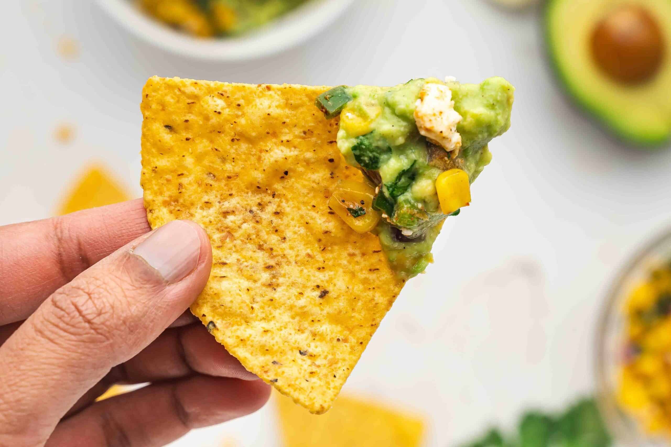 Close-up of a tortilla chip scooping a generous portion of Mexican street corn guacamole.