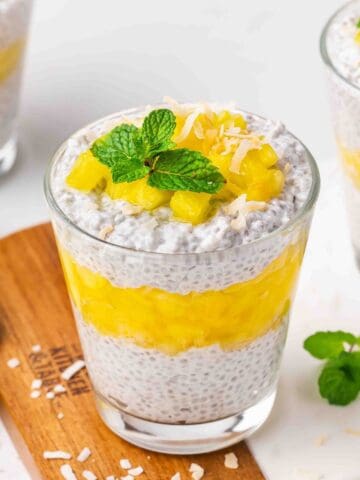 Three neatly layered pineapple chia pudding cups with pineapple pieces and coconut on top.
