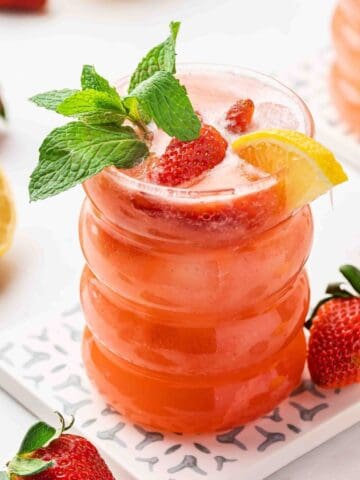 Strawberry lemonade mocktail with mint and lemon garnish on marble surface.