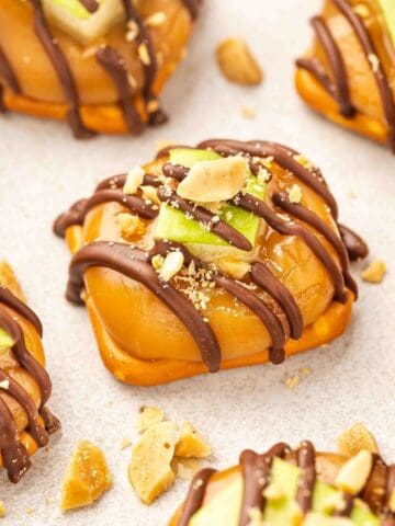 Close-up of caramel apple pretzel bite with chocolate drizzle and peanuts.