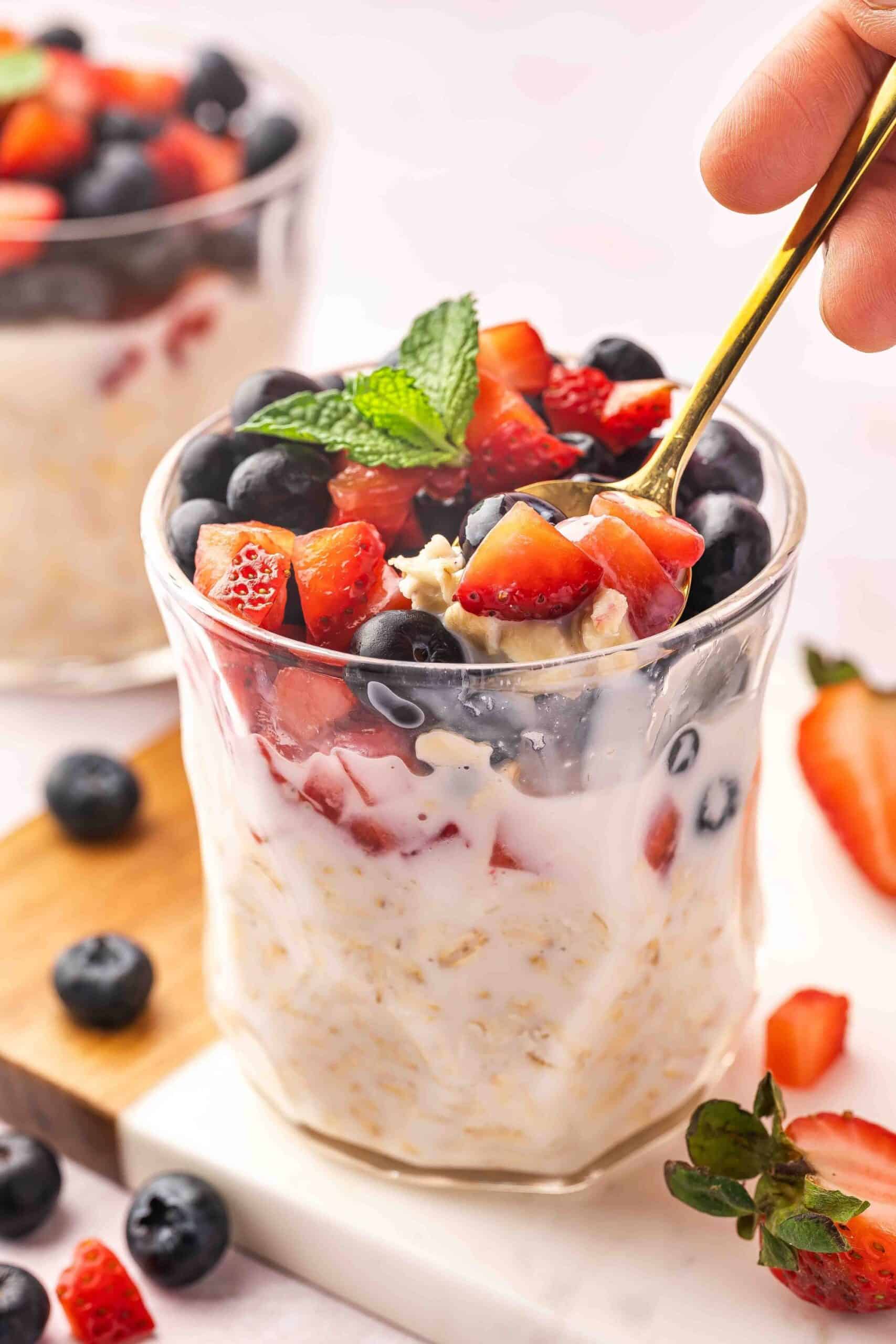 Close-up shot of a spoon in a jar of layered blueberry strawberry overnight oats, showcasing creamy texture.