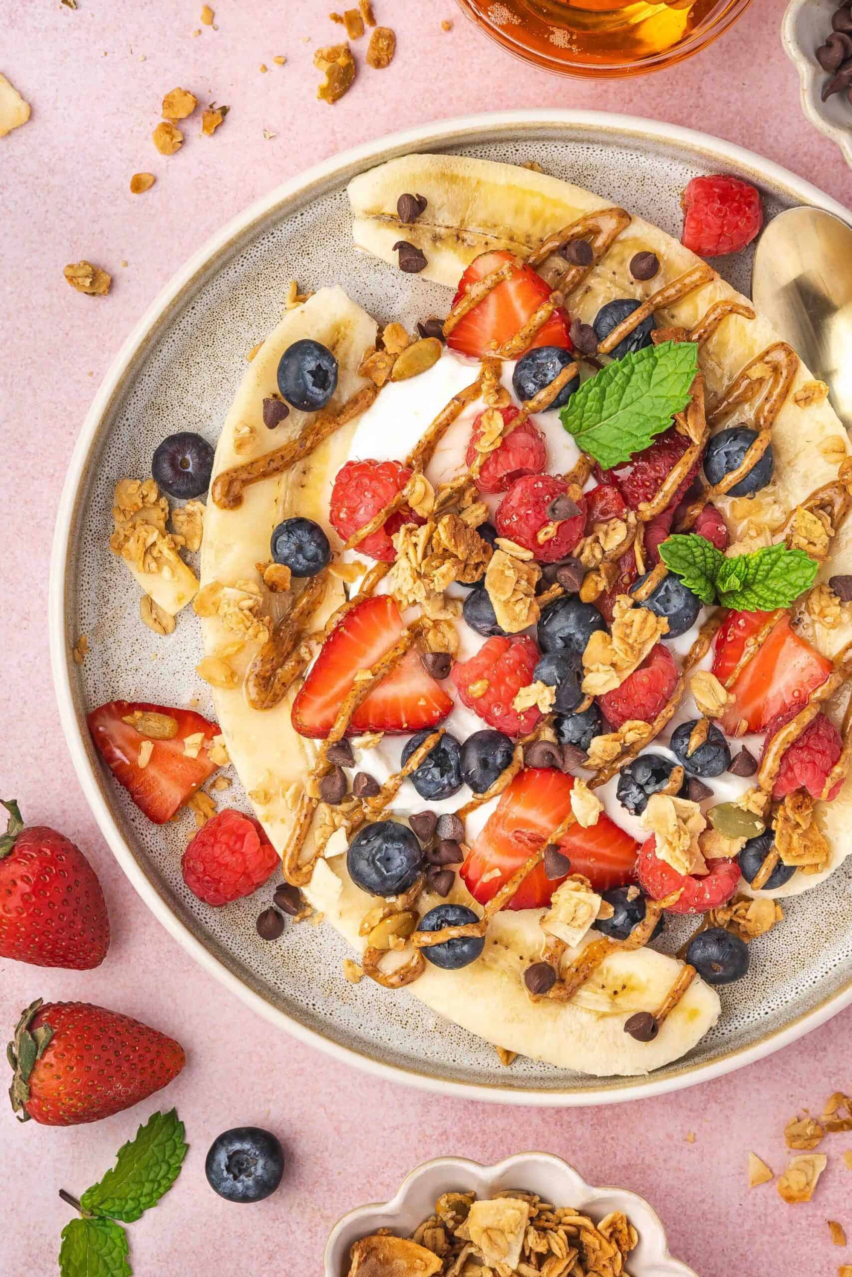 Delicious Greek yogurt banana split topped with fresh berries and crunchy granola.