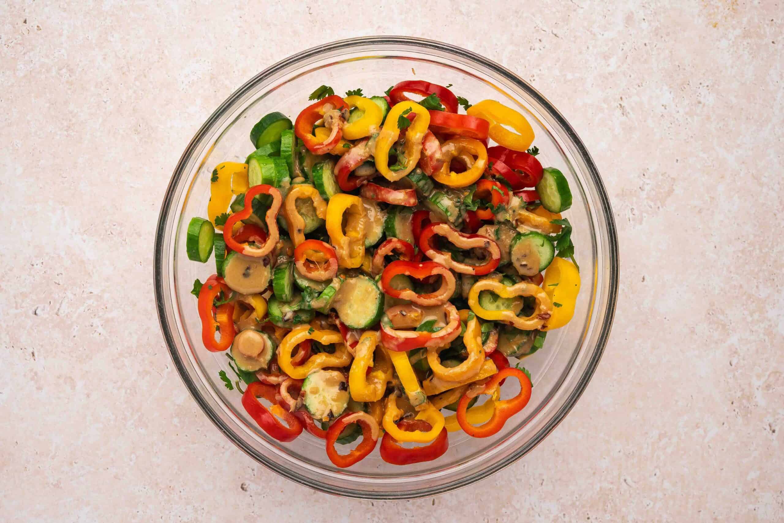 Pouring creamy tahini ginger dressing over cucumber and pepper salad