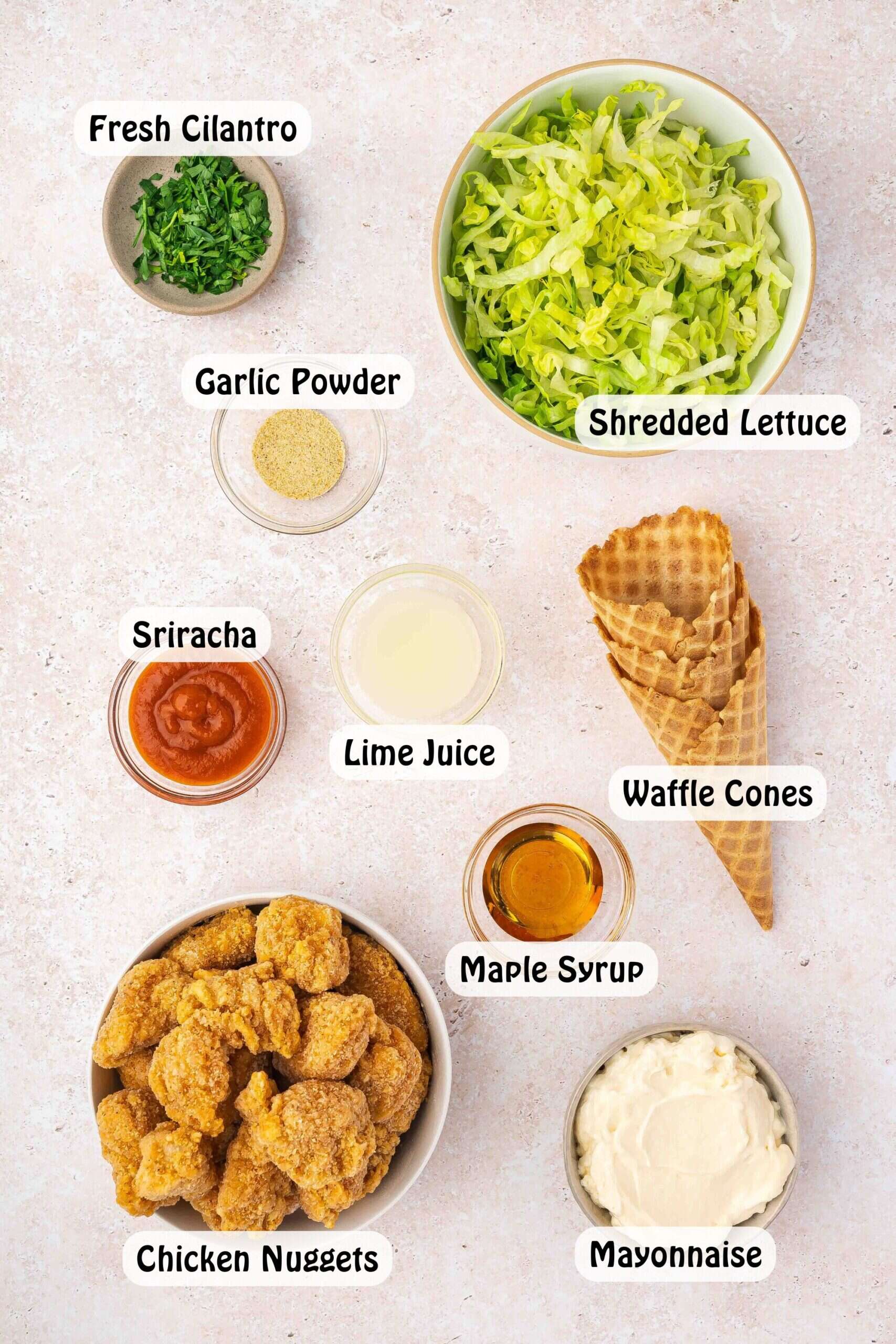 Flatlay of ingredients including waffle cones, chicken nuggets, shredded lettuce, sriracha, mayo, and seasonings arranged on a kitchen surface