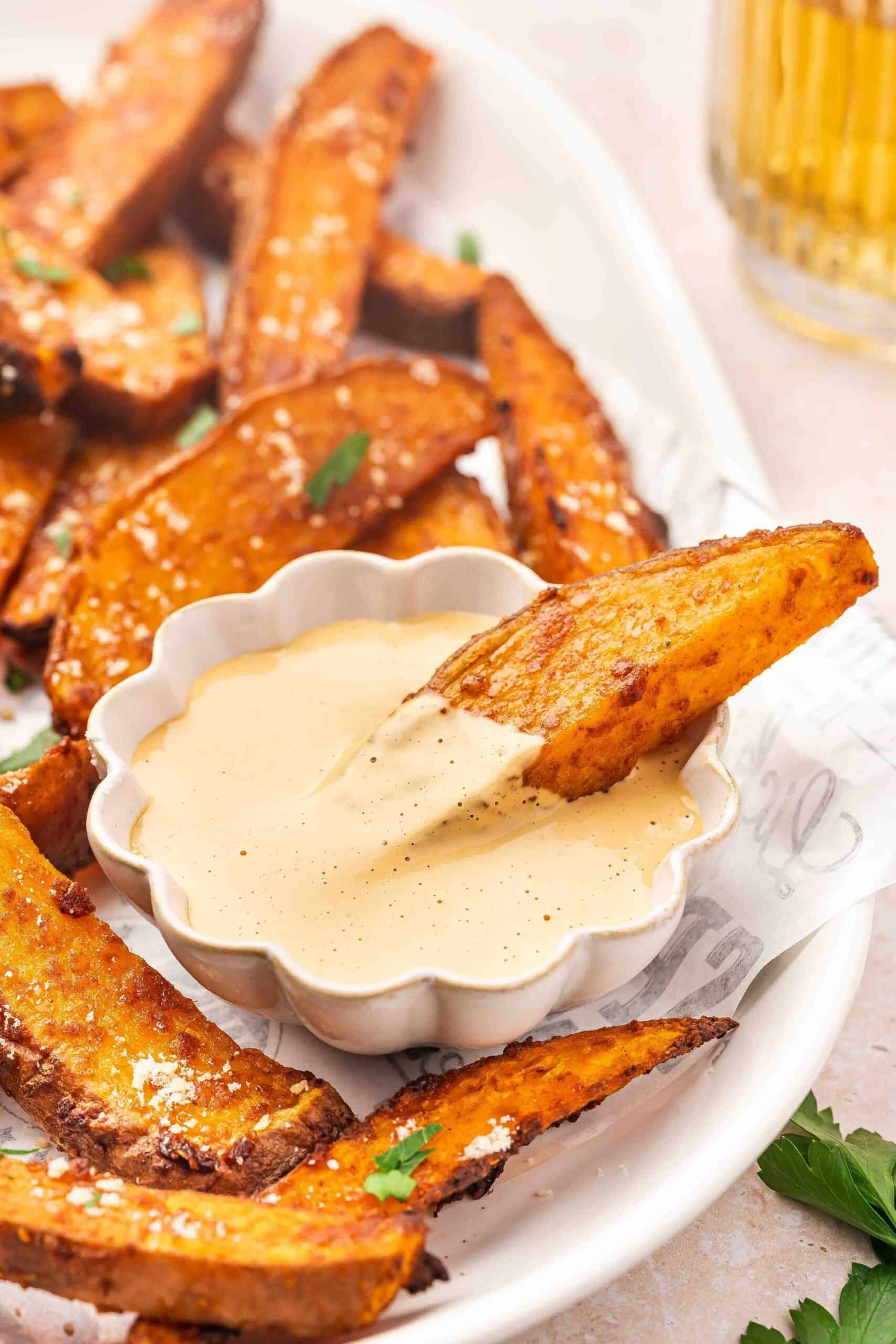 Air fryer sweet potato wedges next to chipotle sauce in a rustic bowl