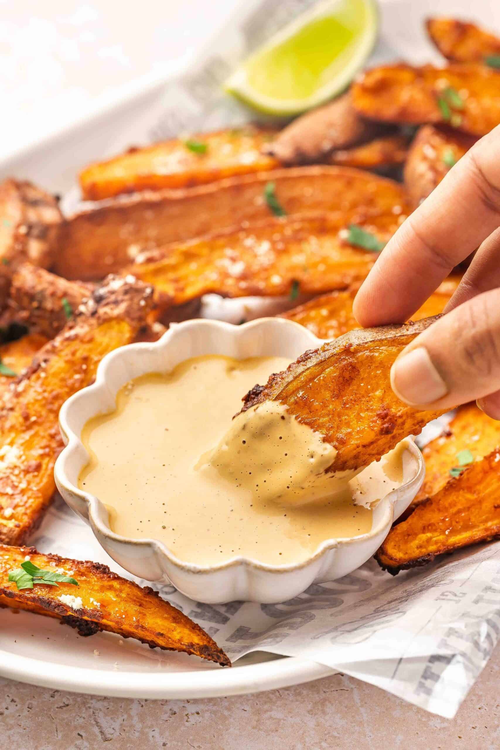 Hand dipping a crispy sweet potato wedge into homemade chipotle sauce