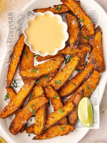 A vibrant plate of crispy air fryer sweet potato wedges garnished with fresh parsley, served alongside a small bowl of creamy homemade chipotle sauce