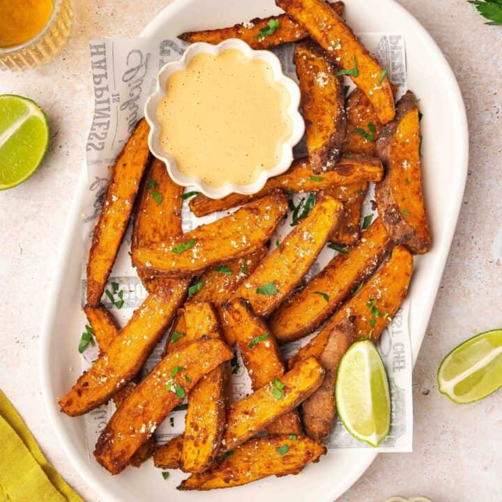 A vibrant plate of crispy air fryer sweet potato wedges garnished with fresh parsley, served alongside a small bowl of creamy homemade chipotle sauce