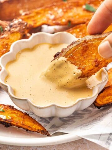 Crispy sweet potato wedge being dipped into creamy homemade chipotle sauce, showing a close-up of the textures