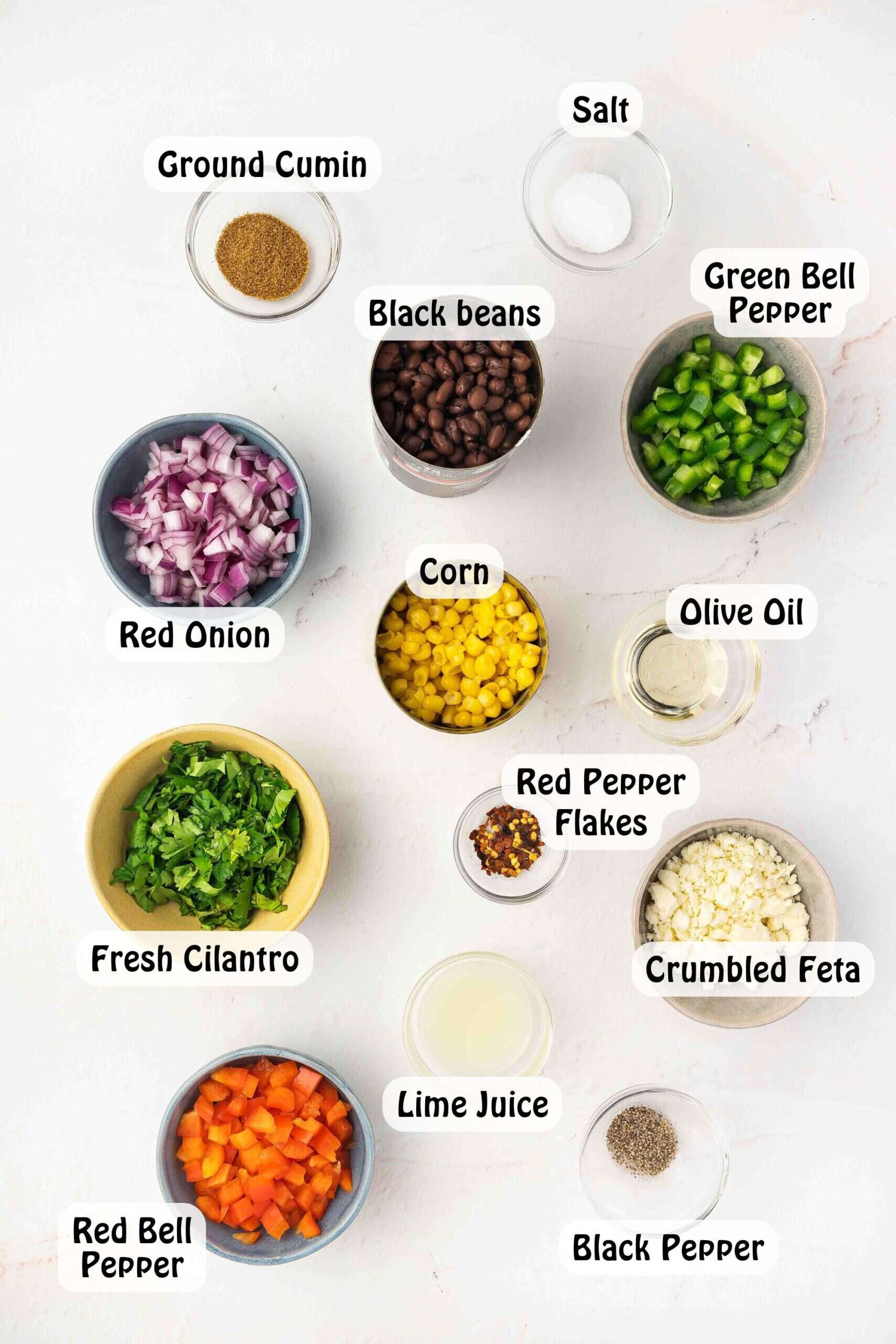 Ingredients for black bean corn feta dip displayed on a white ceramic platter with lime, peppers, and cilantro