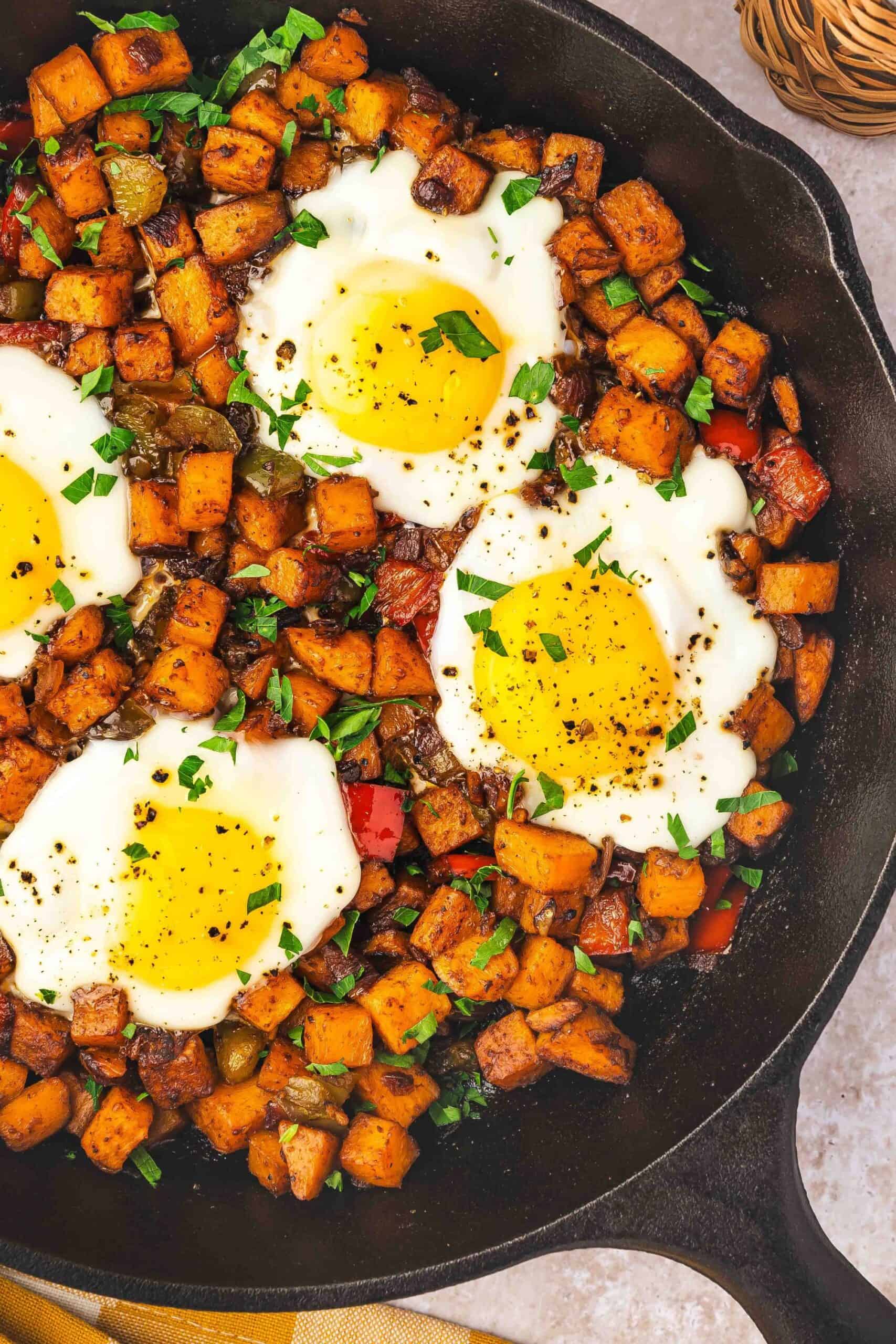 Close-up of crispy golden sweet potato cubes and perfectly cooked eggs in a cast iron skillet, garnished with fresh parsley