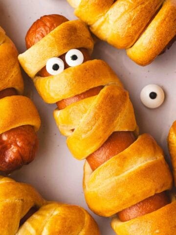 Close-up of a golden Air Fryer Mummy Hot Dog showing crescent roll bandages and candy eyes.