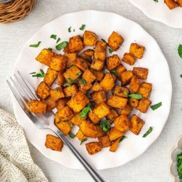 Top view of crispy roasted sweet potatoes served on a white plate with parsley garnish.