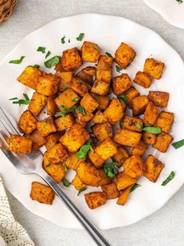 Top view of crispy roasted sweet potatoes served on a white plate with parsley garnish.
