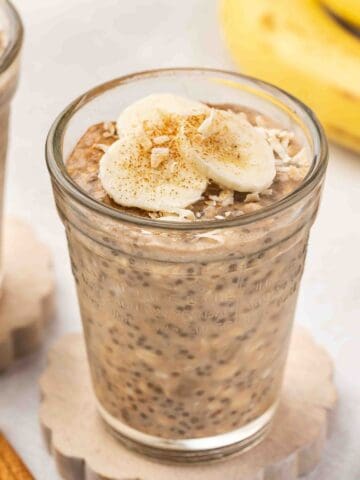 Banana chia overnight oats in a glass cup, topped with banana slices and shredded coconut
