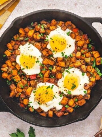 Top-down view of sweet potato breakfast hash with eggs and parsley served in a cast iron skillet