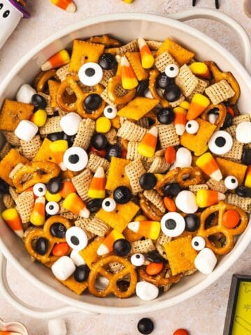 Spooky Halloween snack mix with Chex, Cheez-Its, pretzels, candy corn, marshmallows, and candy eyes in a large ceramic bowl