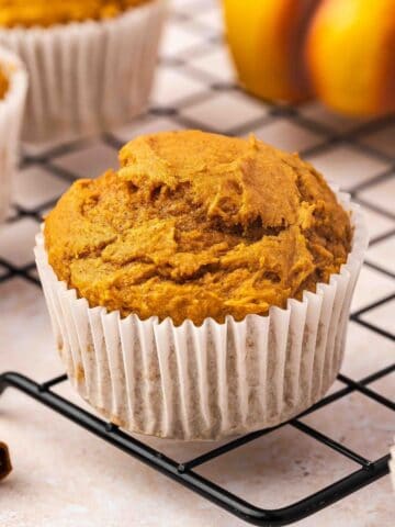 Pumpkin muffins on a wire rack with a few cinnamon sticks and autumn leaves around.