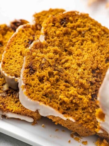 Close-up of moist pumpkin spice bread slices stacked on a ceramic platter, highlighting the crumb texture and pecans