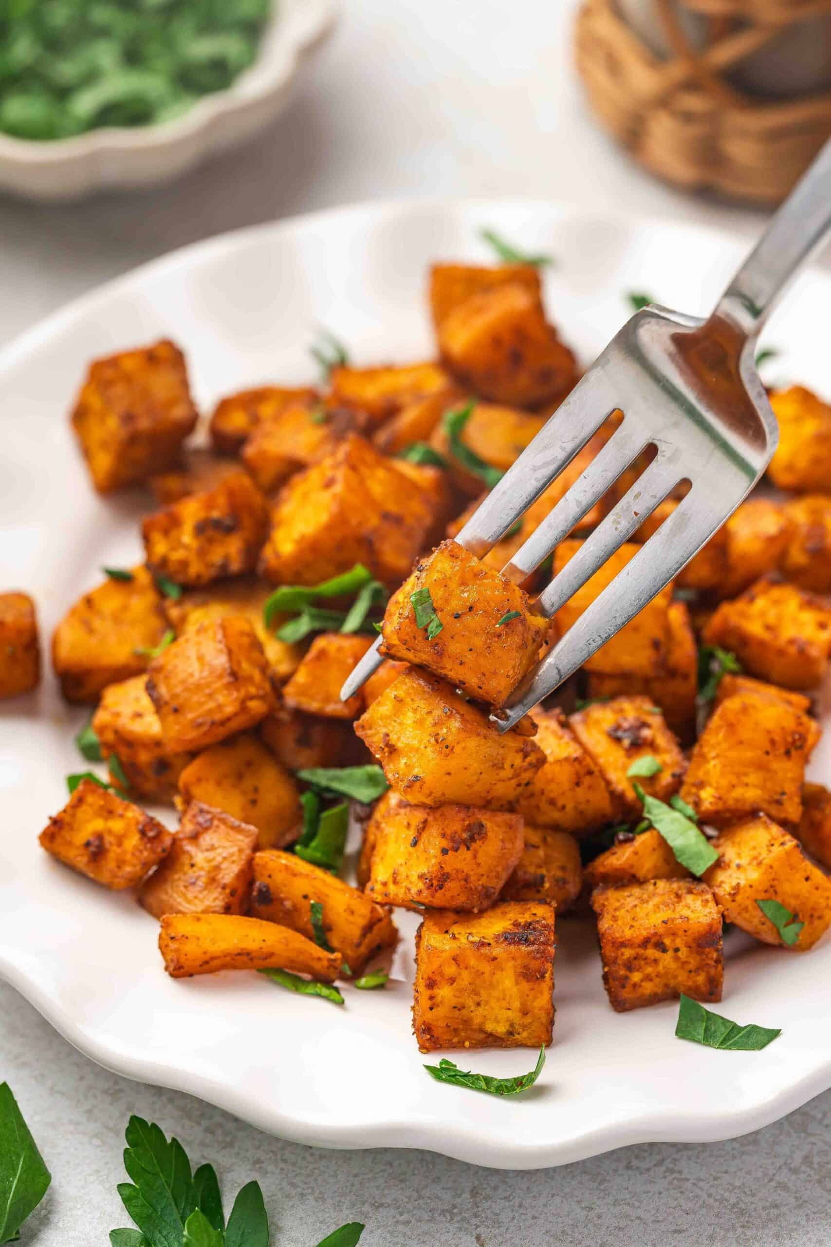 Close-up of crispy roasted sweet potato cubes garnished with chopped parsley on a plate.